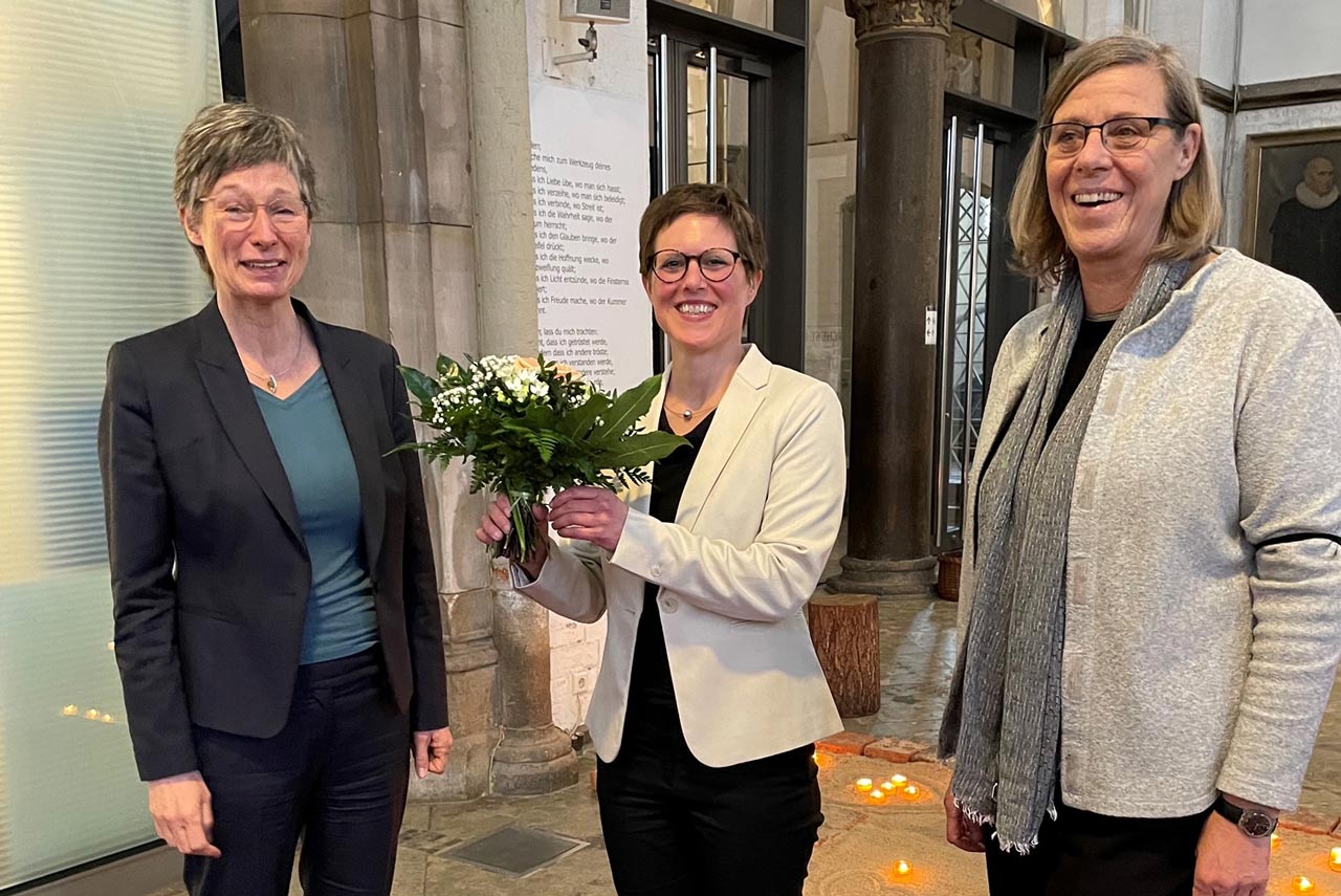 3 Frauen nebeneinander, die mittlere hat einen Blumenstrauß in der Hand